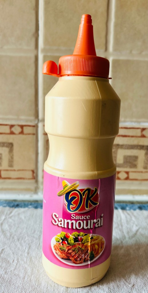 A bottle of Samurai sauce with a pink label featuring a sombrero and a dish of meat and vegetables.